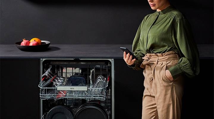Woman in green blouse using phone next to dishwasher